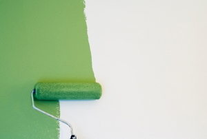 Green paint being applied to an off-white wall with a roller. 
