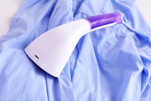 A purple-and-white handheld garment steamer lying on top of a blue shirt.