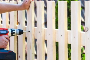 hands with screw gun building wood fence