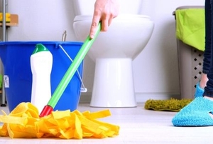 a woman cleaning a bathroom floor with a mop.