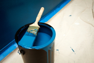 An open can of blue latex paint with a paint brush across the top.