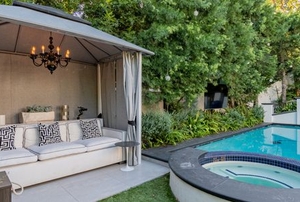 patio cabana with cushions and a chandalier next to a pool
