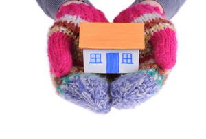 A pair of mittens holds a small cardboard house. 
