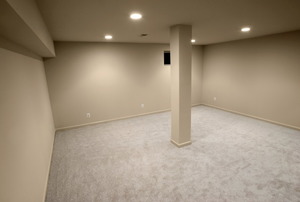 a large room with tan walls, carpet, and a column in the middle