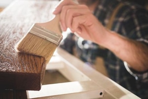 hand with brush applying stain to wood furniture