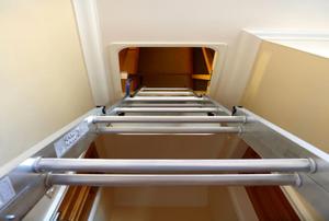 Looking up the rungs of a metal ladder at the attic entrance to which it leads.