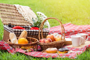 picnic basket and blanket laid out with fruit, donuts, mugs, and bread