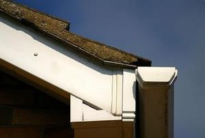A close-up of the corner of a roof, with soffit, shingles, and gutter visible.