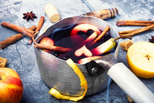 A metal pot with fruit slices and cinnamon sticks in and around it. 