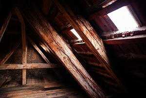 The corner of an old, dimly-lit attic with a couple windows on the near wall.