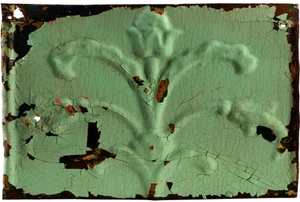 An old, green, tin, decorative tile with a floral design on it.