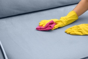 A woman cleaning a couch with water stains.