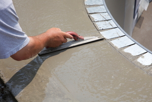 worker repairing pool deck with trowel and concrete