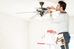 A man works on a ceiling fan light.