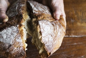 two hands cracking open a fresh loaf of homemade bread