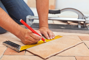 A construction worker measuring a piece of tile. 