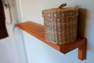 A wicker basket with a lid on a narrow timber shelf in a bathroom.