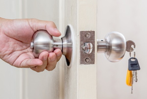 A hand on a doorknob with keys in the lock. 