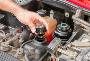 A hand removing the cap to the oil reservoir under the hood of a car. 