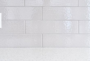 an electrical outlet in a shiny tile backsplash behind a clean countertop