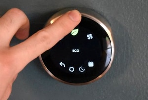 hand touching digital thermostat with leaf and eco icons