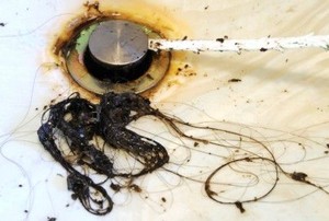 a clump of hair near a drain getting poked with a cleaning device