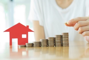 A red paper house next to stacks of coins.
