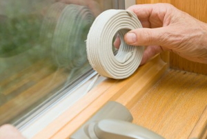 Weatherstripping tape being added around the outside of a window.