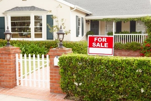 A cottage with a red "for sale" sign in front.