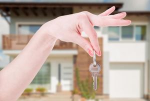 A female hand holding a key with a modern house in the background.