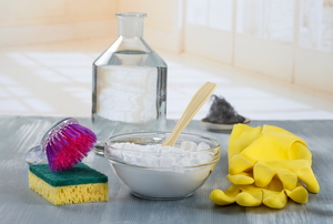 A bowl of baking soda on a grey countertop amongst gloves and other cleaning supplies.