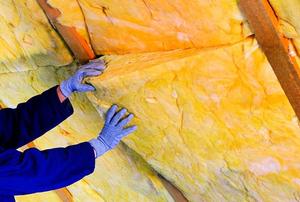 Hands installing a fiberglass batts in the rafters of an attic.
