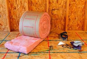 A roll of insulation and some tools in an unfinished room.