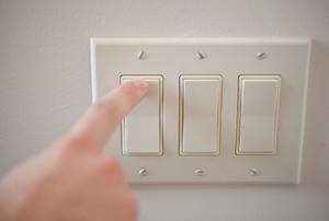A hand turning on a panel light switch.