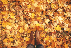 A pile of orange fall leaves and a pair of brow women's boots.