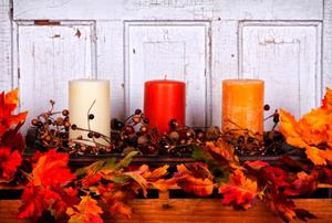 Three candles of white, red, and yellow on a mantlepiece surrounded by fall berries and leaves.