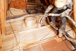 A worker installing white spray foam insulation in an attic.