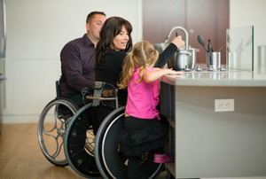 A couple in wheelchairs cooks in an accessible kitchen with their daughter.