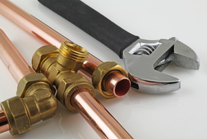 Copper pipes with fittings and a wrench laying on a white surface. 