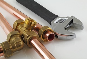 Copper pipes with fittings and a wrench laying on a white surface. 