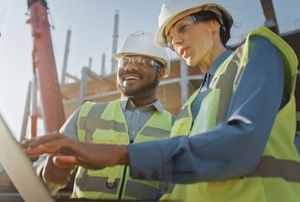 two construction workers with a laptop on a building site