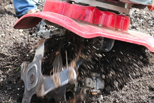 red rototiller with spinning metal digging up dirt
