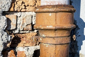 A rusty pipe against a brick wall.