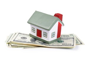 A small toy house with a red door on a stack of cash.