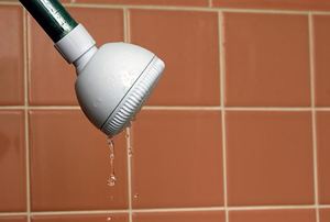 A dripping shower head against an orange tiled shower.