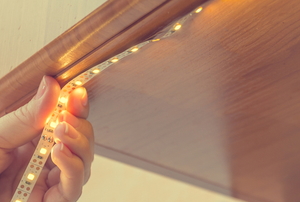 hand attaching long thin strip of LED lights under a cabinet