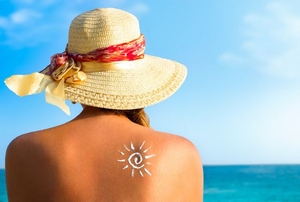 A woman sitting on a beach looking at the water with sunscreen on her back.