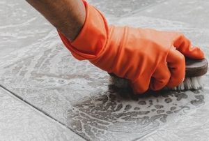 gloved hand scrubbing tile floor with brush