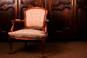 An fancy antique chair against ornately-carved wooden doors.