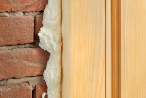 A polyurethane layer squeezing out between a wood frame and a brick wall.